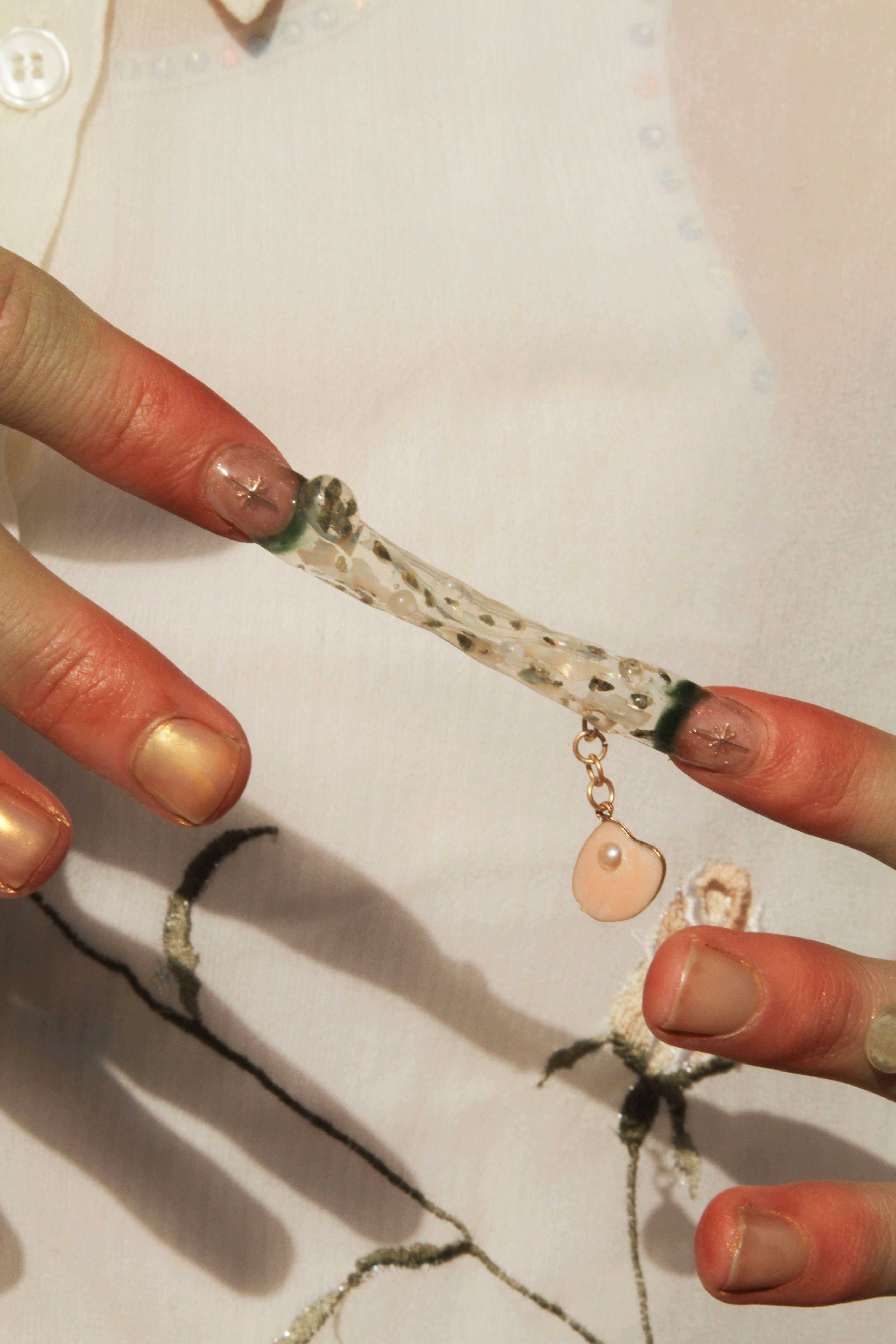Two pointer fingers connected by a transparent nail sculpture full of tiny snails